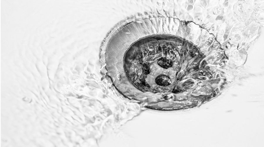 Close-up of a drain with water flowing into it, illustrating the importance of drain cleaning in preventing clogs and plumbing issues.